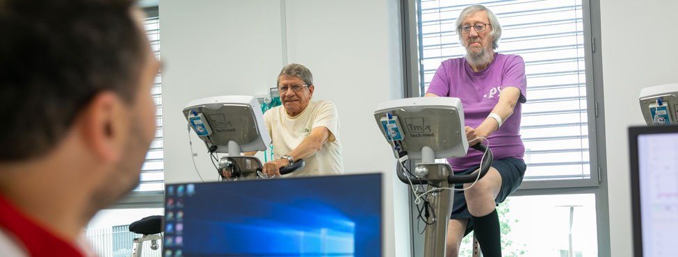 Soignant devant ordinateur surveille patients sur vélos de rééducation à l'effort
